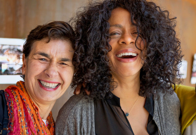 Two attractive older women with their heads together smiling at the camera